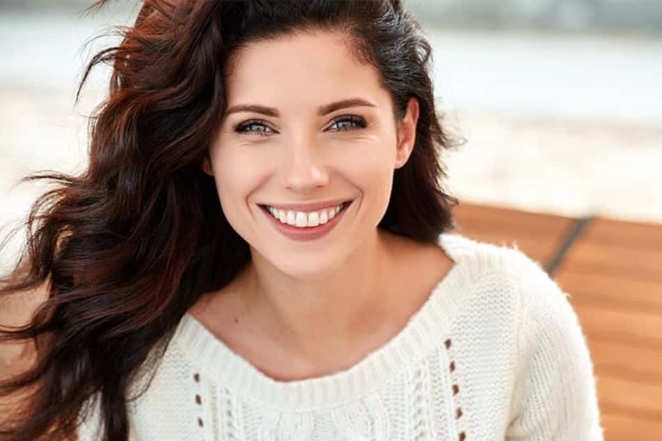 A beautiful, young woman with long, dark hair wearing a white sweater and smiling
